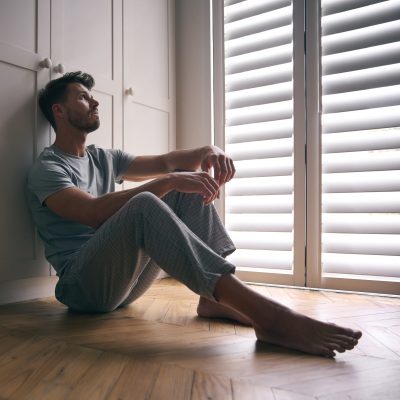 Depressed Man Suffering With Poor Mental Health Sitting On Floor At Home